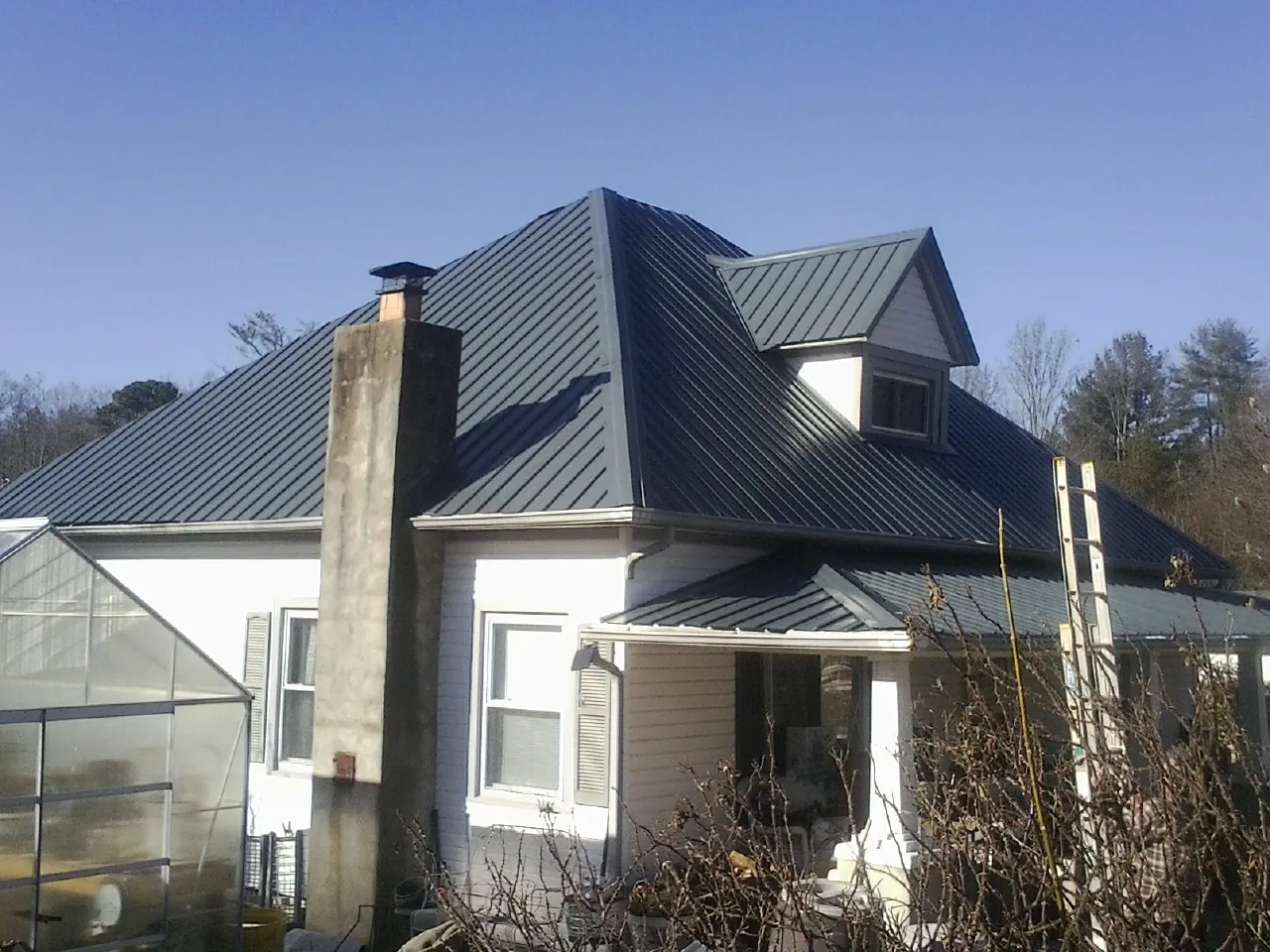 Dark blue standing seam metal roof on a white farmhouse with dormer — Slate & Tile Roof Repair by Roofing Brothers in Summerville