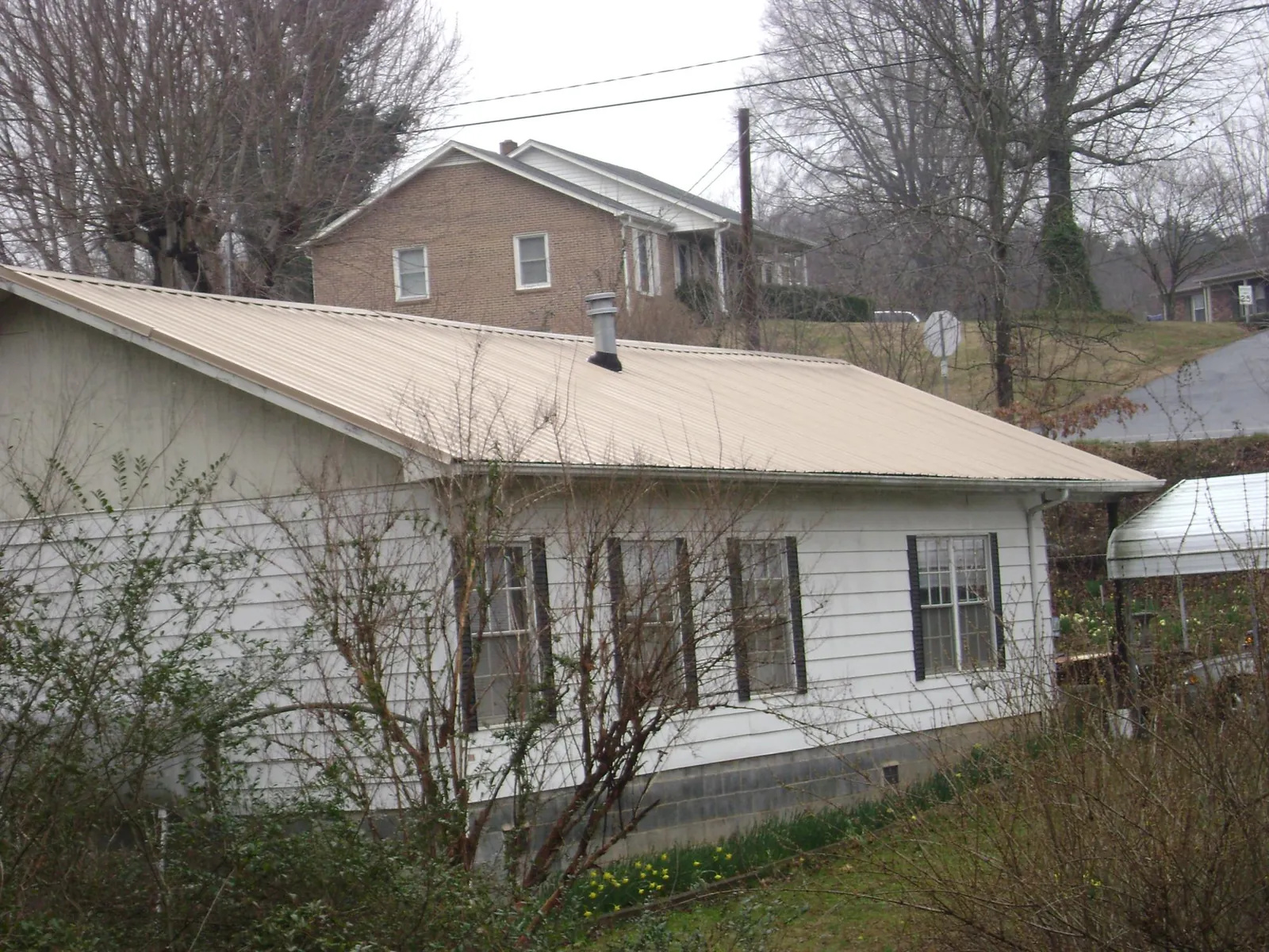 Tan metal roof on a white sided house set into a hillside — Commercial Roofing by Roofing Brothers in Summerville